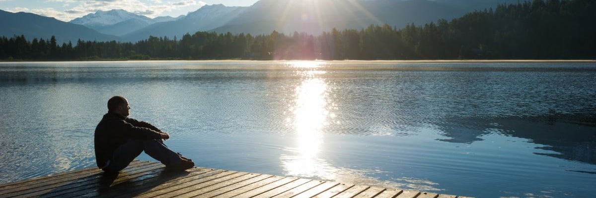 Man-sitting-on-dock-looking-at-mountains